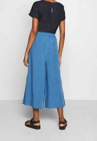 Blue wide-leg culottes with an elastic waistband and side pocket, paired with a black short-sleeve top featuring a back button detail.