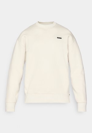 Lichtbeige sweatshirt met een ronde halslijn, ribgebreide mouwen en onderrand, en een klein zwart logo op de borst. Zachte textuur en een relaxte pasvorm.