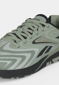 Αθλητικό παπούτσι Reebok φωτεινού πράσινου και μαύρου χρώματος με υφασμάτινη υφή, ζιγκ-ζαγκ σχέδια και χονδρά κορδόνια σε μαύρη και καμουφλάζ σόλα.