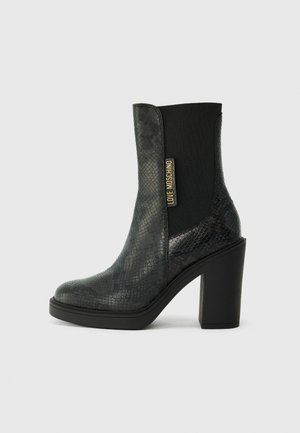 Black ankle boots with a glossy, textured snakeskin pattern, featuring a block heel and elastic side panels with a gold logo accent.