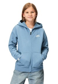 Ljusblå zip-up hoodie med känguruficka, ribbade muddar och nederkant. Har en vit logotyp på bröstet. Bärs över en vit t-shirt.