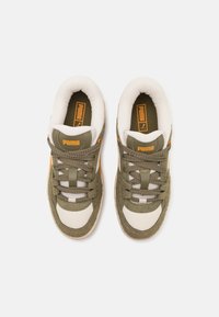 Sneaker verde in suede e bianco in rete con lacci marroni, accenti arancioni e un logo Puma prominente sulla linguetta e sul lato.