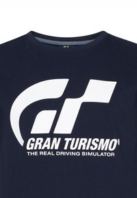 Camiseta de algodón azul marino con un gran logo blanco "GT" que presenta una bandera a cuadros estilizada y el texto "Gran Turismo: El verdadero simulador de conducción."