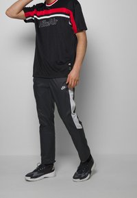 Svart NikeAir t-shirt med röda och vita horisontella ränder; grå träningsbyxor med vita sidopaneler; svarta sneakers med vita detaljer.