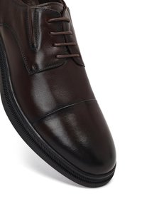 Bruine leren dresschoenen met een gladde afwerking, vijf veterogen en een ronde neus. Voorzien van een rubberen zool met een subtiel patroon.