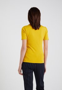 Žlutý top s krátkým rukávem vyrobený ze 100% bavlny, přiléhavý střih, hladká textura. V kombinaci s modrými pruhovanými kalhotami, standardní střih, viditelná postranní kapsa.