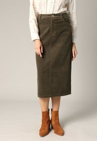 Olijf groene corduroy midi rok met voorzakken, knoopsluiting en gemêleerde stof. Gekoeld met bruine suède enkellaarsjes.