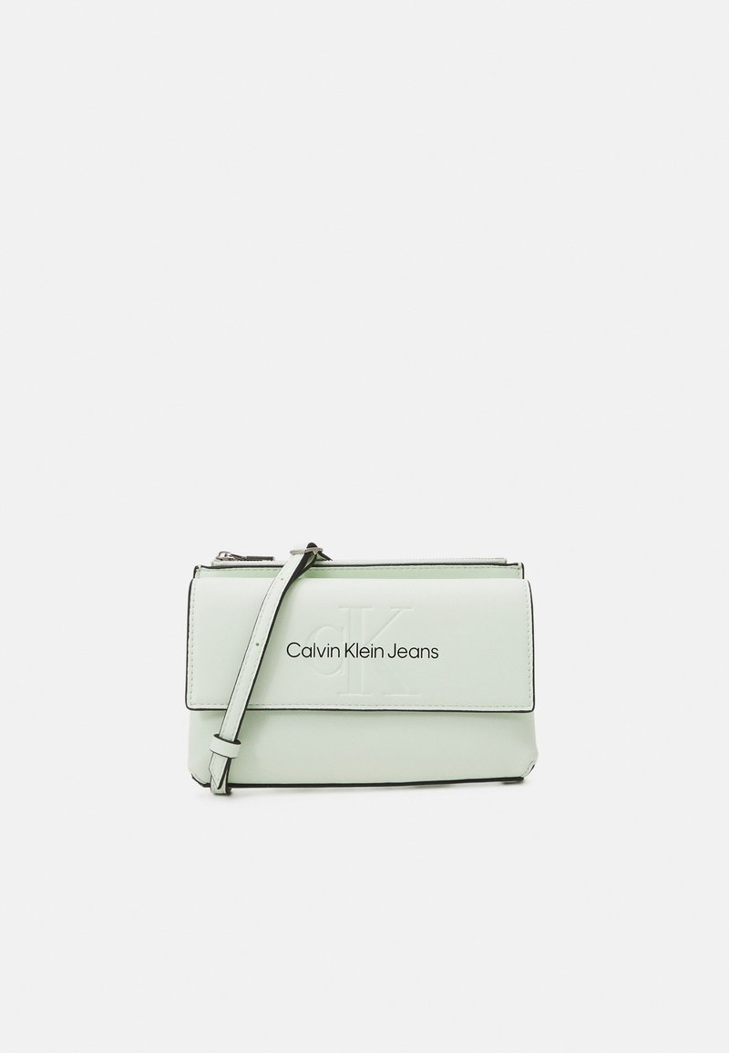 Jasnozielona skórzana torebka z klapą na zakładkę, odpinanym paskiem i wytłoczonym logo "Calvin Klein Jeans" z przodu.