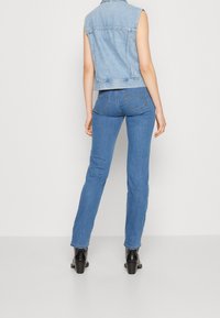 Ljusblå denimjeans med slim fit, avsmalnande ben och subtila sömnadsdetaljer. Matchas med en ärmlös denimväst. Svarta klackstövlar är synliga.