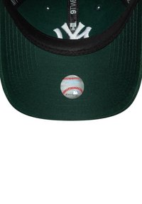 Grünes Baseballcap mit schwarzem Schirm, das ein erhabenes weißes Logo und einen runden MLB-Aufkleber auf der Unterseite des Schirms hat.