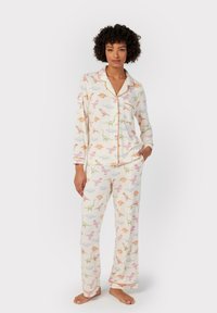 Langarm pyjama set in crème met een kleurrijke dinosaurussen print. Voorzien van contrasterende bies, een notch kraag en relaxte broek.
