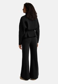 Crna kratka majica s peplum detaljem, uparena s širokim crnim hlačama. Izrađena od mekog tkanja, pokazuje glatku teksturu.