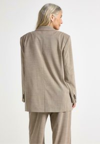 Lys beige blazer med løs pasform, slagkrave og lange ærmer. Tekstureret stof med et subtilt ternet mønster; rygslidsdetalje.