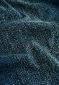 Tumed sinine denim pehme, tekstureeritud pinnaga. Kangas näitab klassikalist twill-kudumismustrit ja nähtavaid õmblusi.