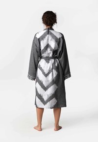 Šedý župan s čierno-bielym cik-cak vzorom na zadnej strane, s dlhými rukávmi a viazaným pásom, vyrobený z textúrovanej tkaniny.