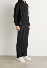 Sudadera con capucha negra con bolsillo delantero, pantalones negros y zapatillas blancas. Incluye un bolso bandolera negro con correa. Diseño sencillo.