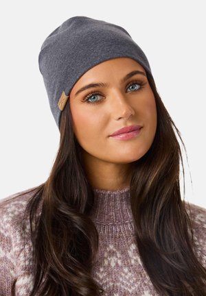 Gray knit beanie with a soft texture, featuring a sewn-on leather label. The model wears a light purple patterned sweater.