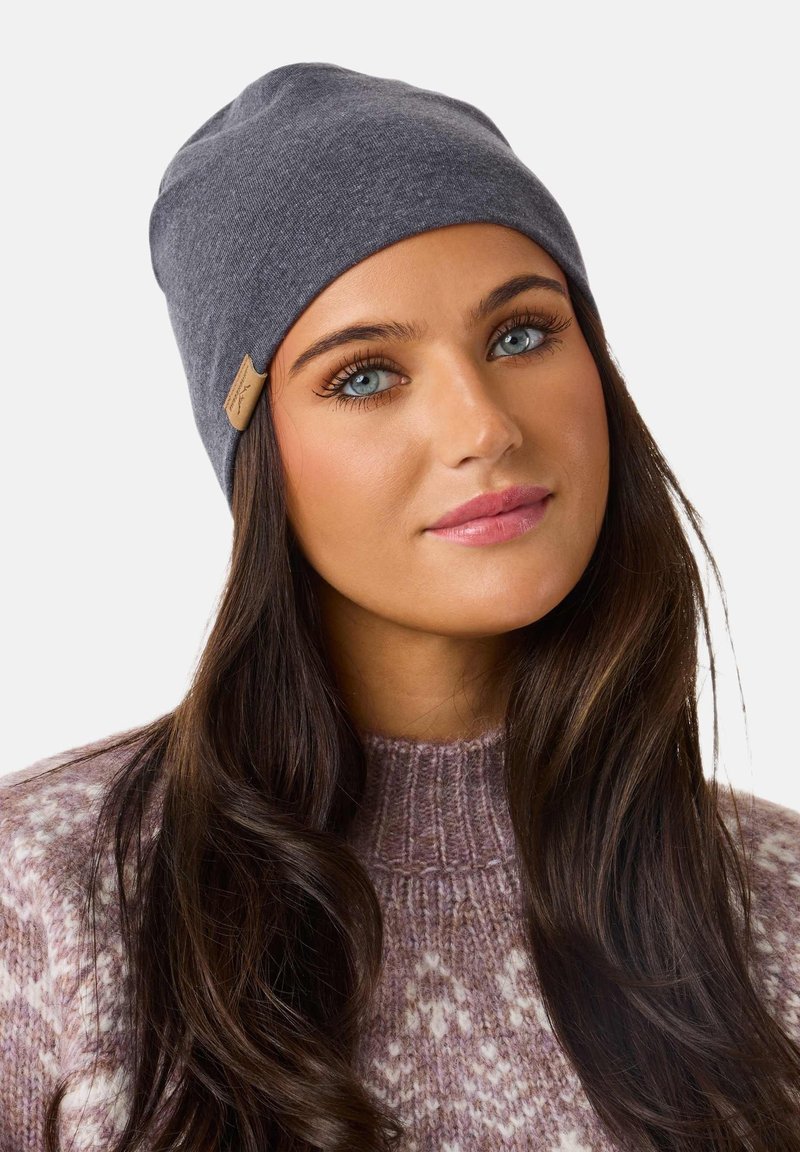 Gray knit beanie with a soft texture, featuring a sewn-on leather label. The model wears a light purple patterned sweater.