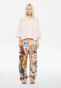 Light beige, short-sleeved shirt with a collar and button closure. Colorful, patterned wide-leg pants featuring abstract designs in orange, blue, and cream.