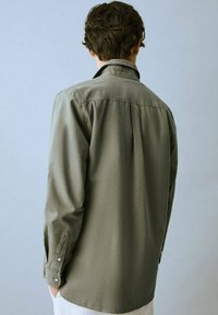 Overmaatse olijfgroene blouse met een zachte textuur, met knoopmanschetten en een achterkant met plooi. Heeft een gekleed halsuitsnijding en een relaxte pasvorm.