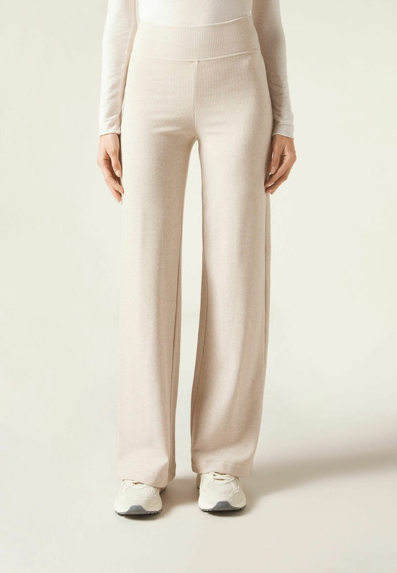 Pantalons côtelés beige clair avec une taille haute, des jambes larges et une texture douce, associés à des baskets de sport légères.