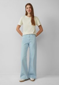 Hellgelbes Baumwoll-T-Shirt kombiniert mit hellblauen Schlagjeans. Das Outfit zeichnet sich durch ein schlichtes Design mit minimalen Akzenten und einer lockeren Passform aus.