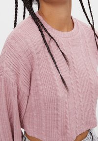 Maglione cropped rosa chiaro con un design a treccia testurizzato, caratterizzato da un colletto a girocollo a coste e maniche ampie.