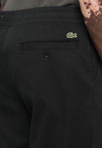 Black shorts with a textured finish, featuring an elastic waistband, back pocket with button closure, and a small embroidered logo.