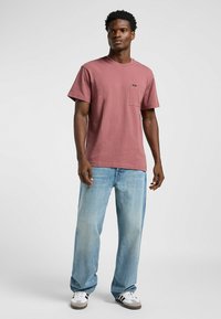 Rosa bomull t-shirt med bröstficka, avslappnad passform, kombinerad med ljusblå denimjeans och svart-och-vita sneakers.