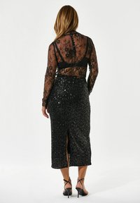 Sorter bluse i sort blonde med lange ærmer og knaplukning, parret med en sort midi-nederdel med pailletter, der har en slids bagpå, samt strophæle.