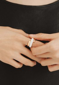 Anillo de declaración en oro y blanco con un acabado suave y brillante, adornado con pequeños strass y un diseño geométrico distintivo.