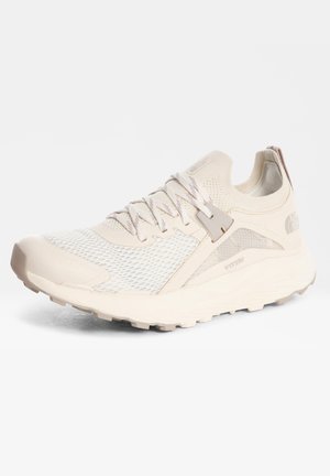 Lyse beige atletiksko med netoverdel, snørelukning og robust sål, designet til udendørs brug og komfort.