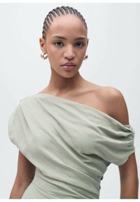 Off-the-shoulder, light green dress made of soft, textured fabric, featuring draped details and gathered sections. Gold hoop earrings accent the look.