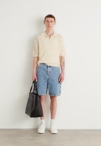 Strikket kremfarget polo skjorte, denimshorts, hvite sneakers og en svart totebag. Enkel design med en avslappet passform.