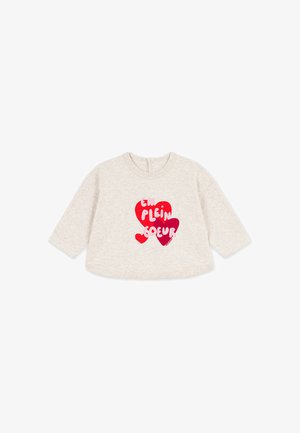 Cremefarbenes Baby-Langarmshirt mit drei roten Herzen und französischem Text "EN PLEIN COEUR" auf der Vorderseite.