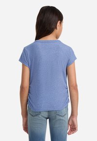 Modra prilegajoča majica s kratkimi rokavi, izdelana iz mehkega materiala. Ima ovratnik v obliki črke U in subtilne nabiranje na straneh.