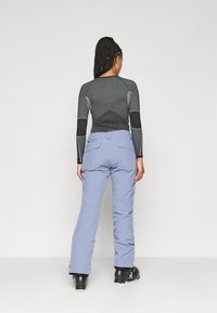 Pantaloni de zăpadă albaștri cu talie ajustată, picioare drepte și buzunare. Asortați cu un top negru cu mâneci lungi, care are accente texturate contrastante.