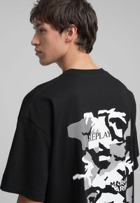T-shirt nera a maniche corte con un grande design grafico bianco sul retro. Realizzata in cotone, con una vestibilità comoda e scollatura rotonda.