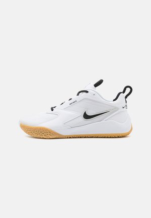 White athletic shoe with a textured upper, black Nike logo, and gum rubber outsole. Features a pull tab and adjustable laces for fit.