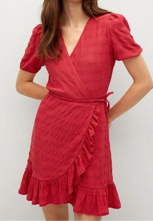 Vrouw draagt een rode wikkeljurk met textuur, korte pofmouwen, een V-hals, ruches aan de zoom en een tailleband om te strikken.