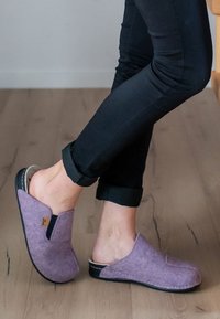 Lila Filzclogs mit offener Rückseite, ausgestattet mit einem strukturierten Obermaterial, schwarzer Gummisohle und einem kleinen Logo an der Seite.
