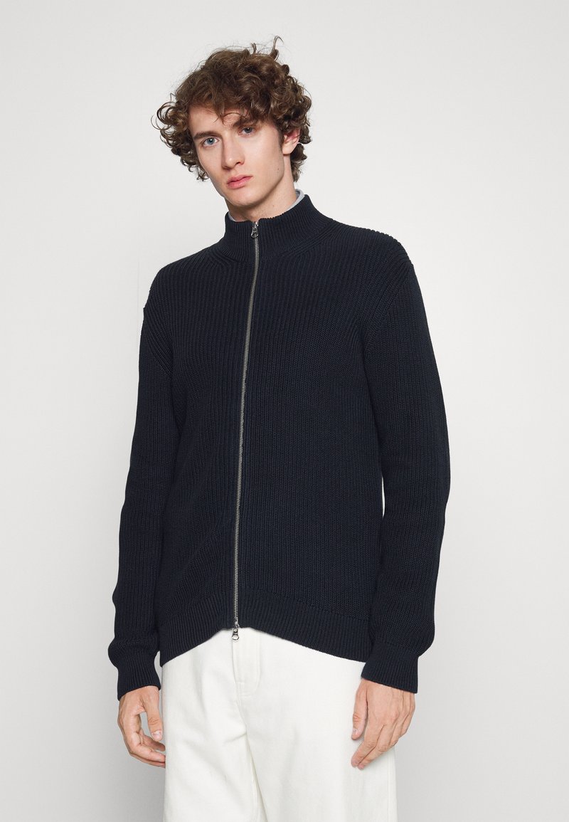 Sudadera azul marino con cremallera, con una textura acanalada, cuello alto y mangas largas, presentada sobre un fondo neutro con un corte recto.