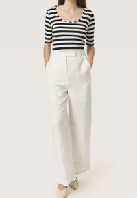 Top aderente a righe bianche e nere con maniche corte, abbinato a pantaloni bianchi in lino a vita alta e a gattini beige con punta appuntita.