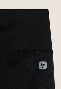 Leggings de fitness negras fabricadas con un tejido texturizado, que cuentan con un parche de logo en un cuadrado gris en la cintura. Material suave y elástico.