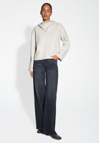 Felpa cappuccio beige chiaro con maniche ampie, abbinata a jeans larghi scuri. Tessuto liscio e silhouette casual, con tasca laterale.