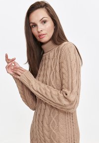 Beiges Strickkleid mit dickem Rollkragen und langen Ärmeln. Verfügt über ein Zopfmuster und Rippdetails entlang des Ausschnitts und der Bündchen.