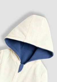 Svetlo béžová mikina na zips s modrou textúrovanou podšívkou v kapucni. Má mäkkú tkaninu a minimálne švy, navrhnutú pre pohodlie.