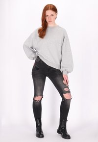 Szürke, oversized pulóver texturált felülettel, lőve a megkopott fekete skinny farmernadrággal és fekete bokacsizmával.