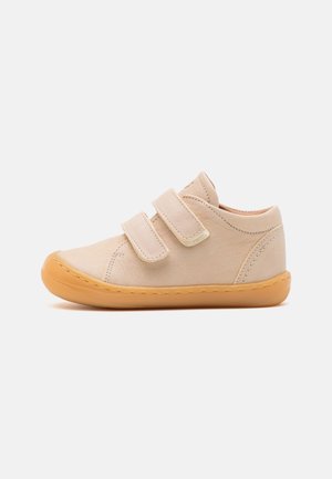 Beige børnesneaker med to justerbare velcroremme og lys brun gummisål, set fra siden på en hvid baggrund.
