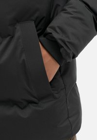 Giacca imbottita nera con una texture liscia e lucida. Presenta una tasca laterale e dettagli con polsini elasticizzati per una vestibilità sicura.